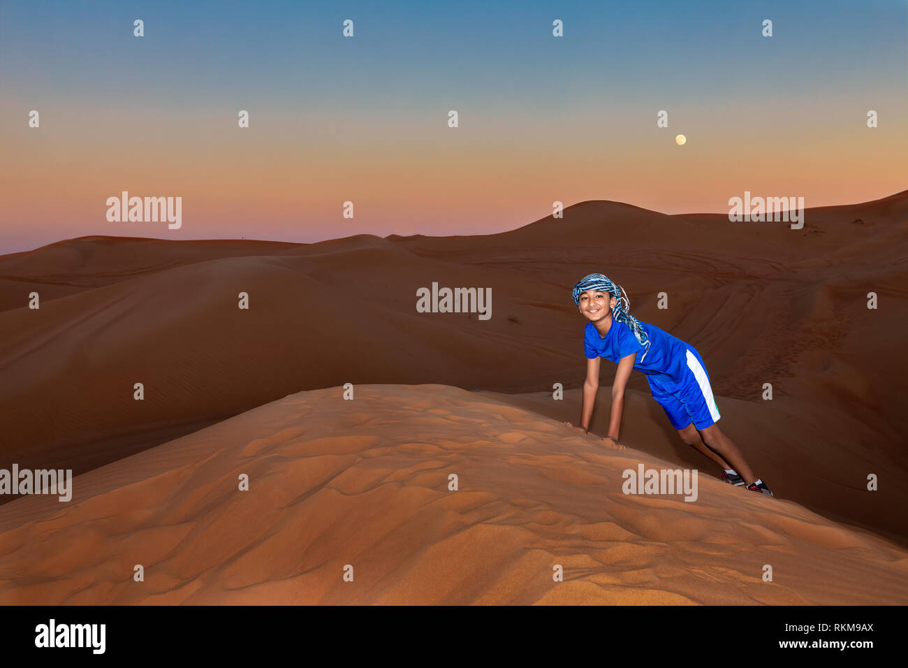Jeune garçon portant un casque d'Oman et à jouer dans les dunes de sable de Dubaï, aux Émirats arabes unis, au coucher du soleil Banque D'Images