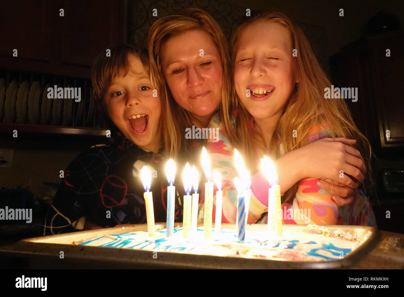 Une fille d'anniversaire ferme les yeux pour faire un voeu avant de souffler les bougies du gâteau d'anniversaire de rage tandis que sa mère et son frère. Banque D'Images