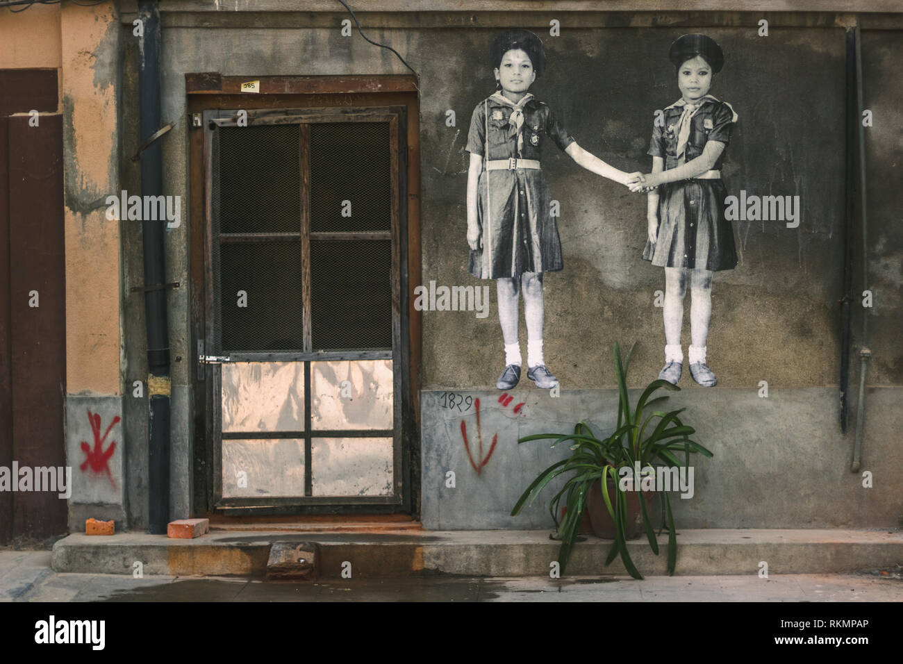 Un mur ayant une oeuvre de deux filles se tenant la main et une plante dans un vase à l'extérieur Banque D'Images