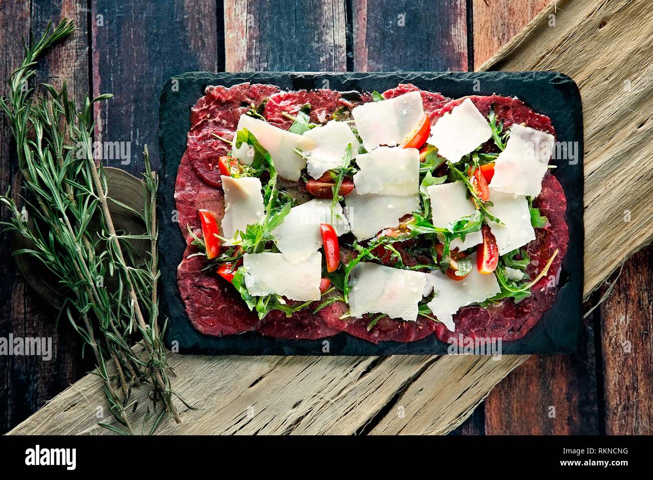 Carpaccio de bœuf frais avec parmesan rasé, piment et salade de roquette sur une photo à plat Banque D'Images