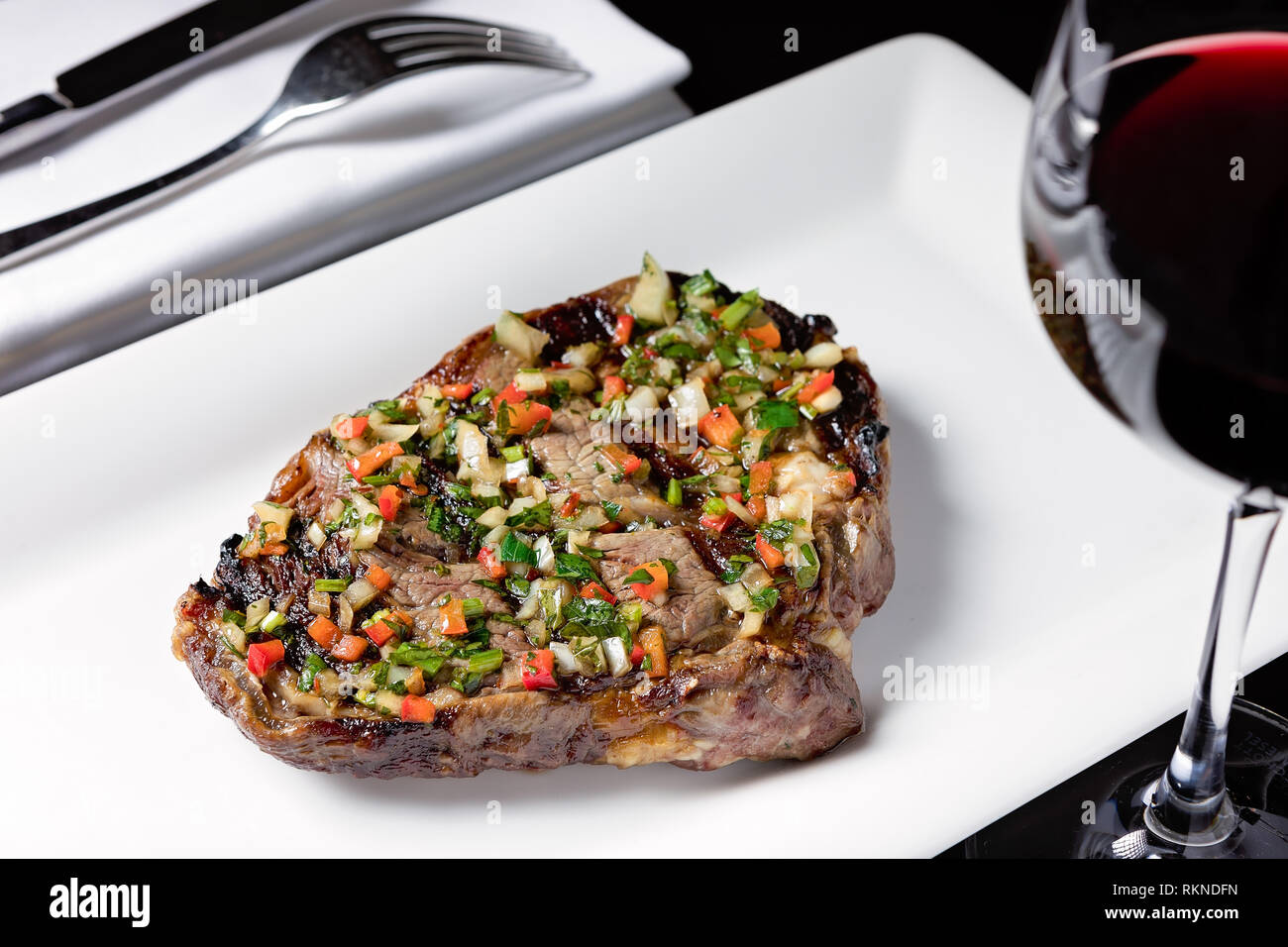 Steak grillé servi sur une assiette blanche finement hachée légumes et un verre de vin rouge Banque D'Images