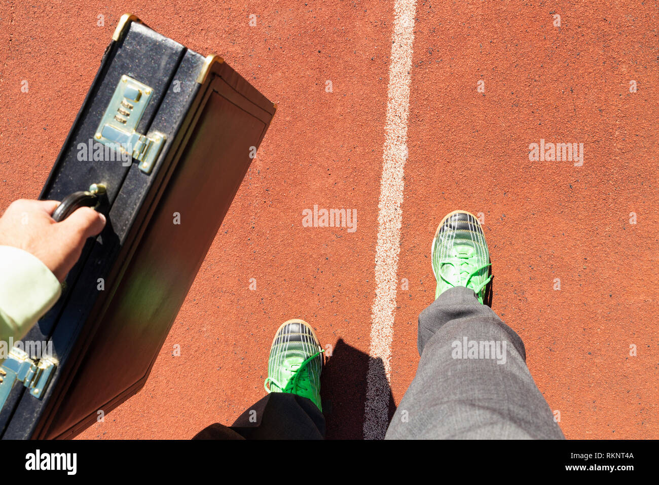 Un homme d'affaires en costume gris avec chemise verte, porte-documents noir et vert chaussures de course debout sur une piste de course. Banque D'Images