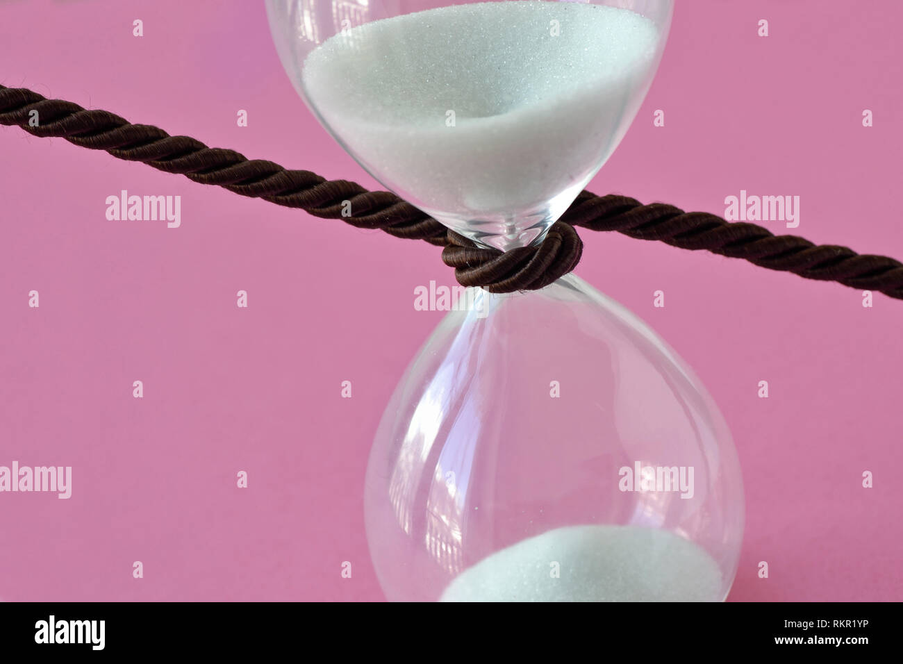 Close-up de hourglass avec un cordon autour d'elle sur fond rose - Arrêter le concept de temps Banque D'Images