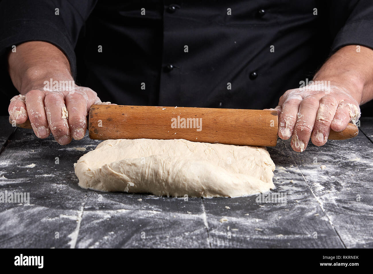 Chef dans une tunique noire roule une pâte pour une pizza ronde, Close up Banque D'Images