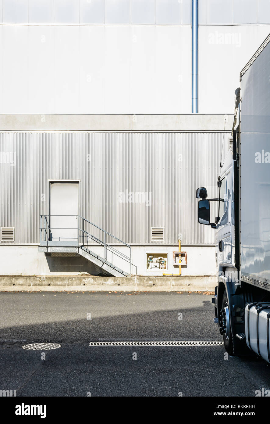 Semi-remorque d'un camion garé en face d'un bâtiment industriel recouvert d'un revêtement en tôle ondulée, gris, avec une porte en haut d'un petit escalier. Banque D'Images