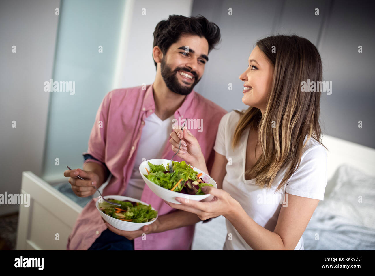 Belle jeune playful couple eating salad ensemble à la maison Banque D'Images
