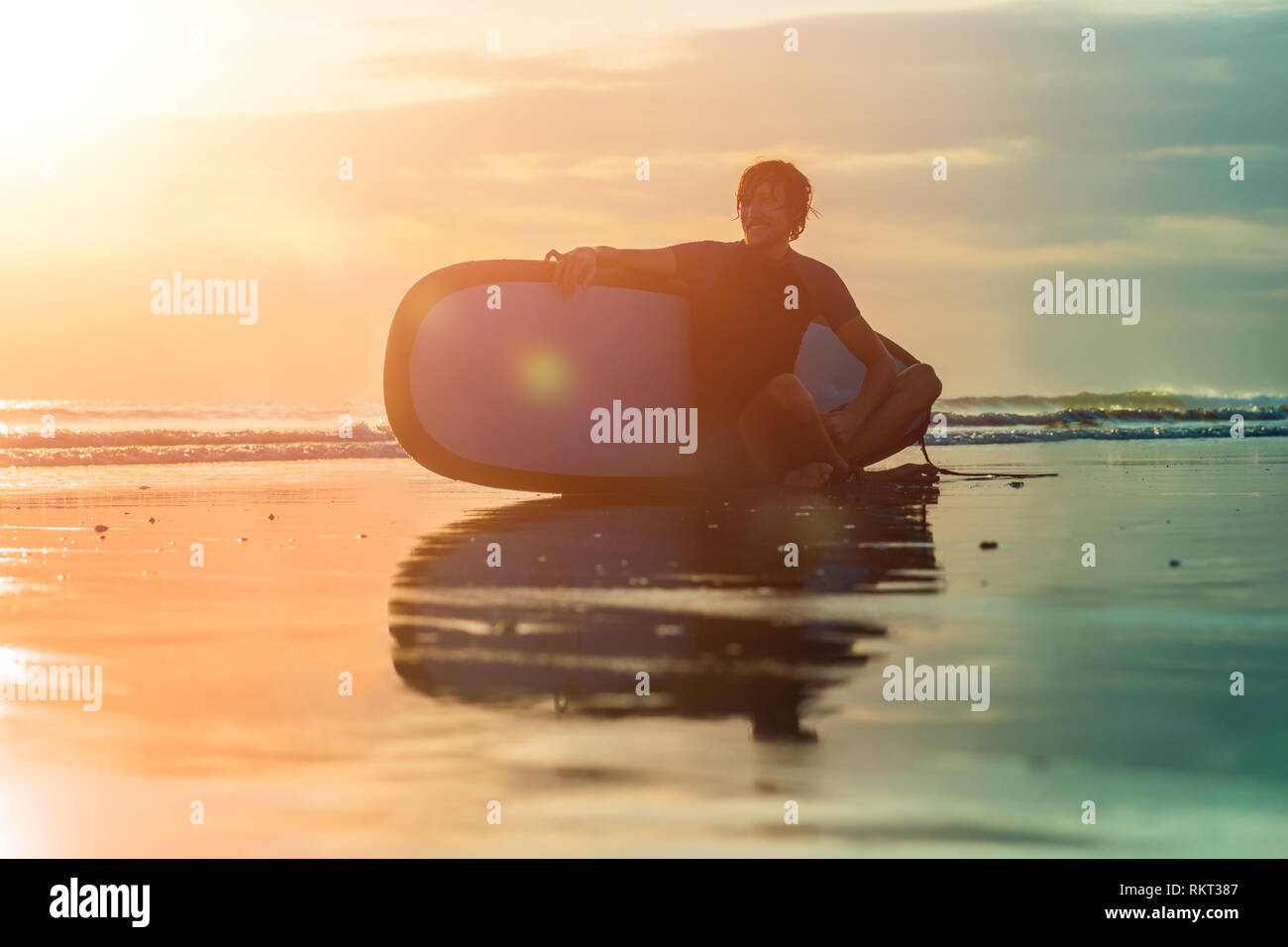 Silhouette de surf homme assis avec un surf sur le bord de la plage à l'heure du coucher du soleil Banque D'Images