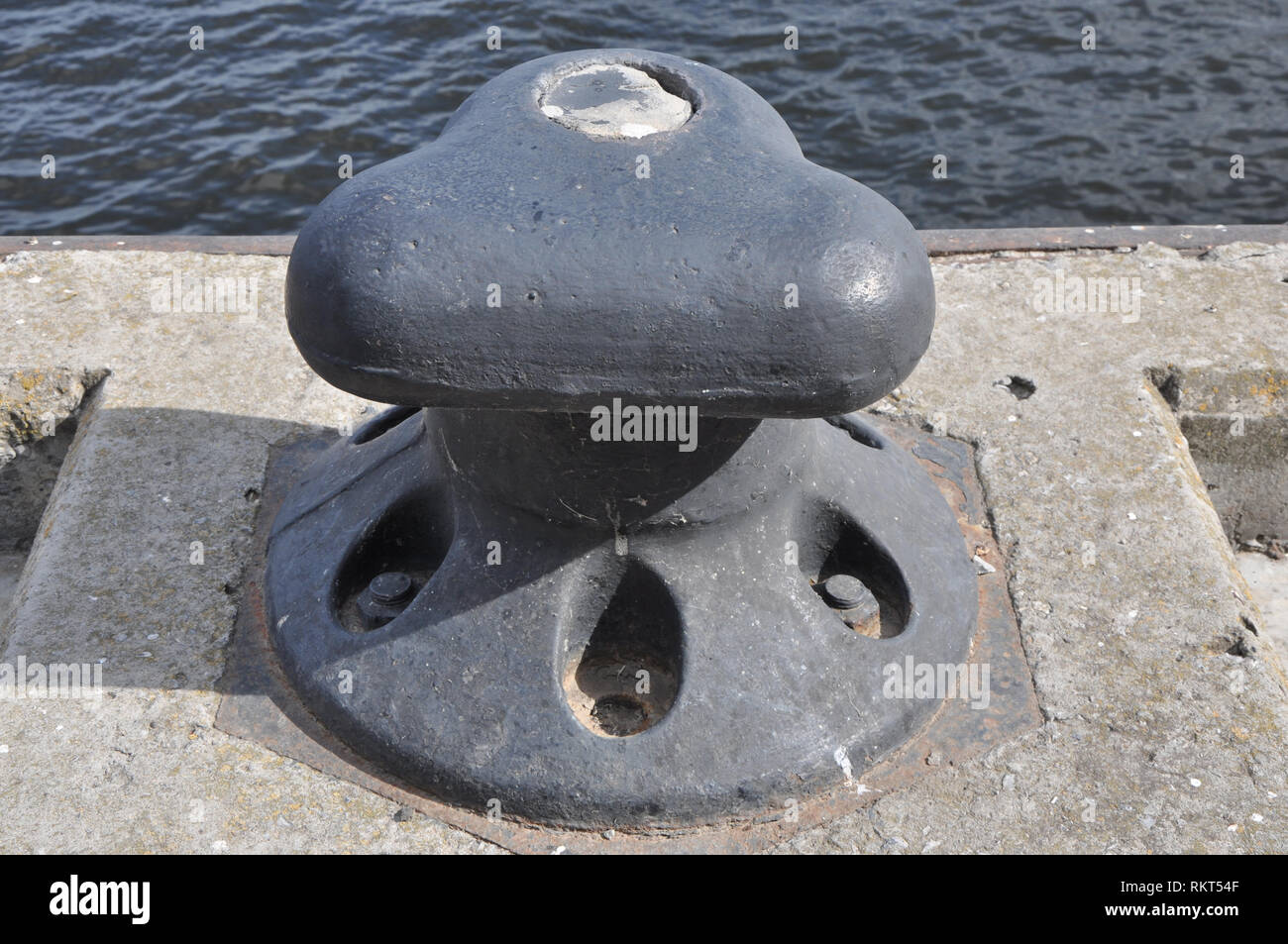 Quai fonte bollard contre rusty le béton et l'eau sombre des vagues. Banque D'Images