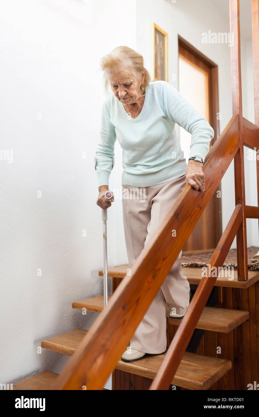 Femme âgée à la maison à l'aide d'une canne pour descendre les escaliers Banque D'Images