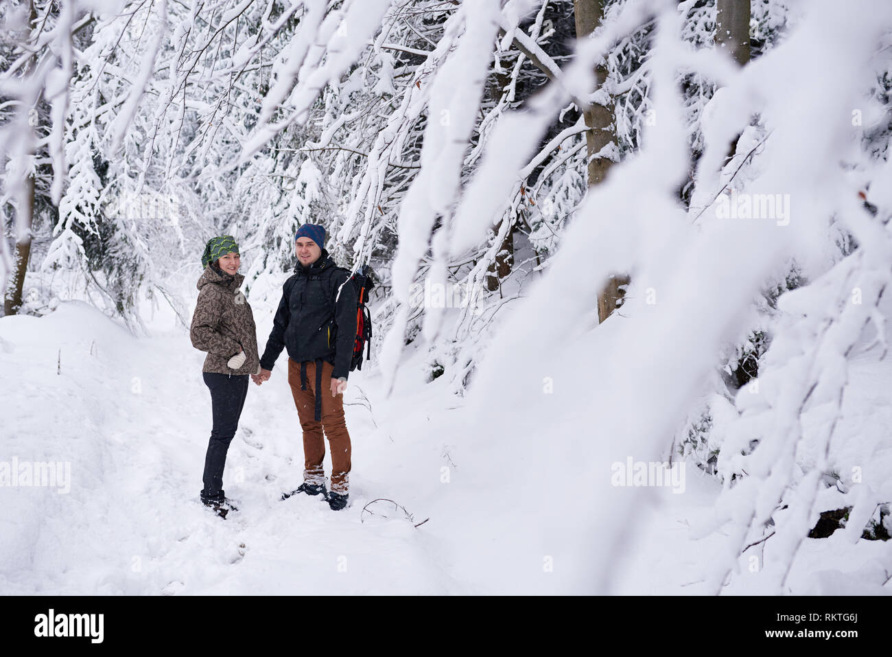 Portrait of a smiling young couple en tenant la main d'équipement de randonnée dans une forêt couverte de neige tandis que dehors pour une randonnée d'hiver Banque D'Images