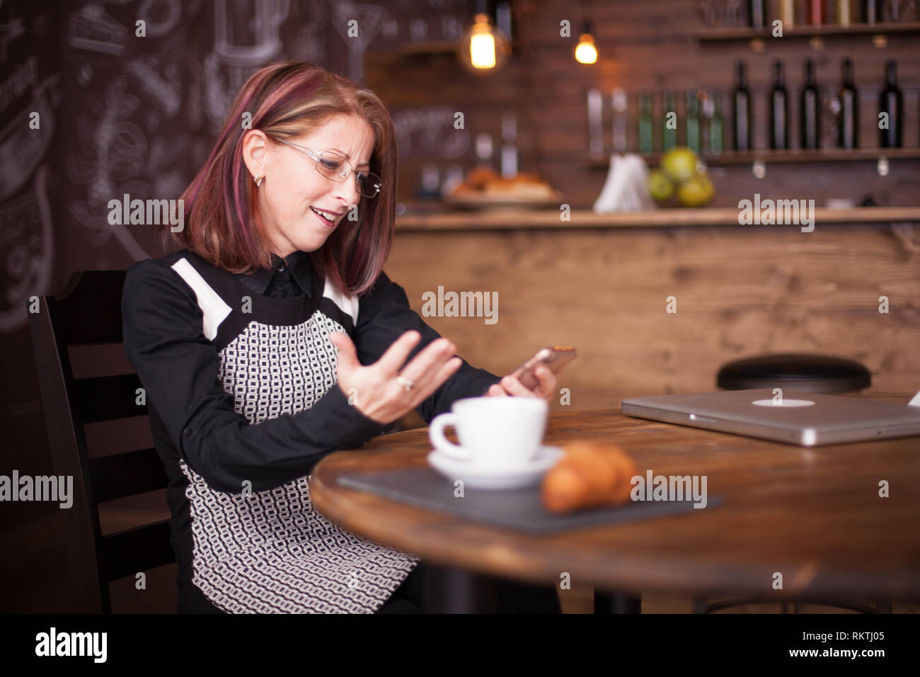 Adult businesswoman étonné tout en utilisant son téléphone à côté de l'anglais un croissant. Belle pub vintage Banque D'Images