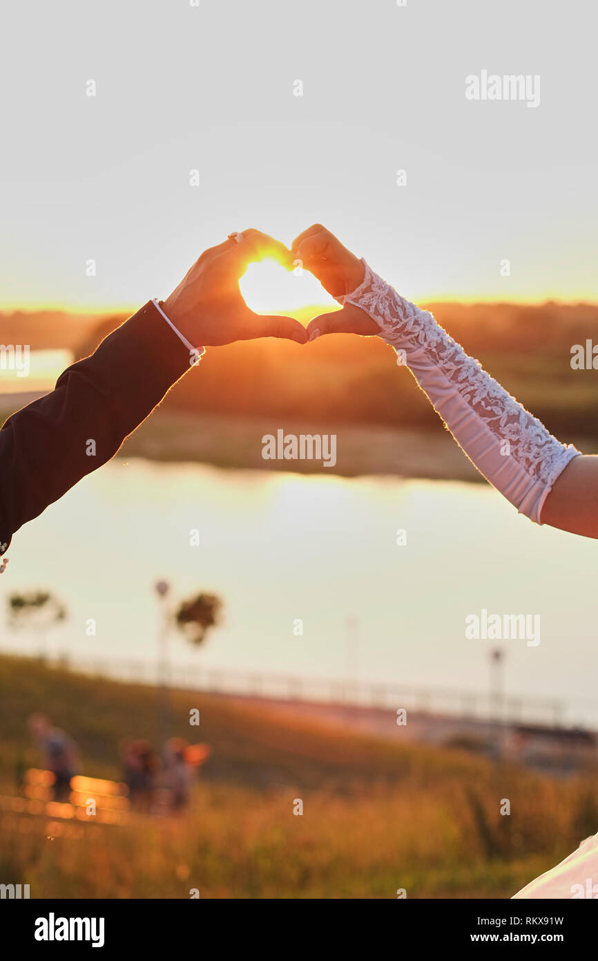 Couple de mariage mains de toucher des doigts dans la forme . La lumière vive du soleil sur l'arrière-plan. Banque D'Images