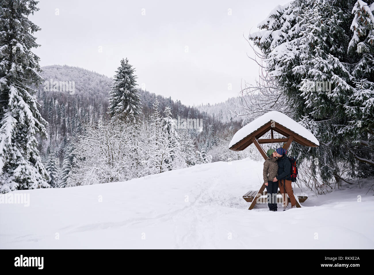 Friends en matériel de randonnée s'embrasser tout en se tenant par un abri dans une clairière couverte de neige tandis que dehors pour une randonnée d'hiver ensemble Banque D'Images
