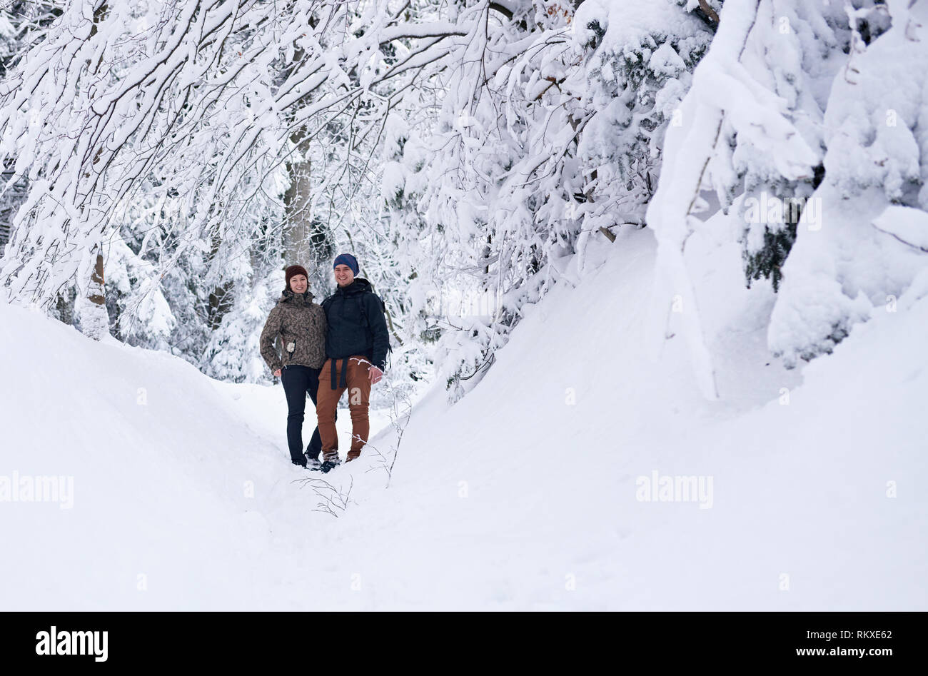 Portrait of a smiling young couple in hiking gear debout ensemble sur un sentier de neige dans une forêt en hiver Banque D'Images