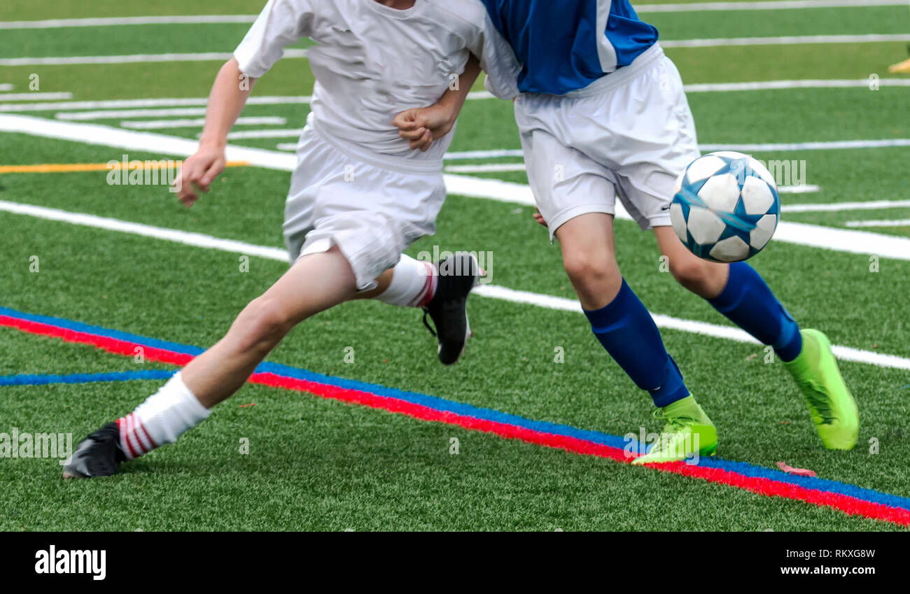 Deux joueurs de football masculin se battent pour la balle durant un match de football. L'un est dans un uniforme blanc et tho autre est dans un haut bleu et un short blanc. Banque D'Images