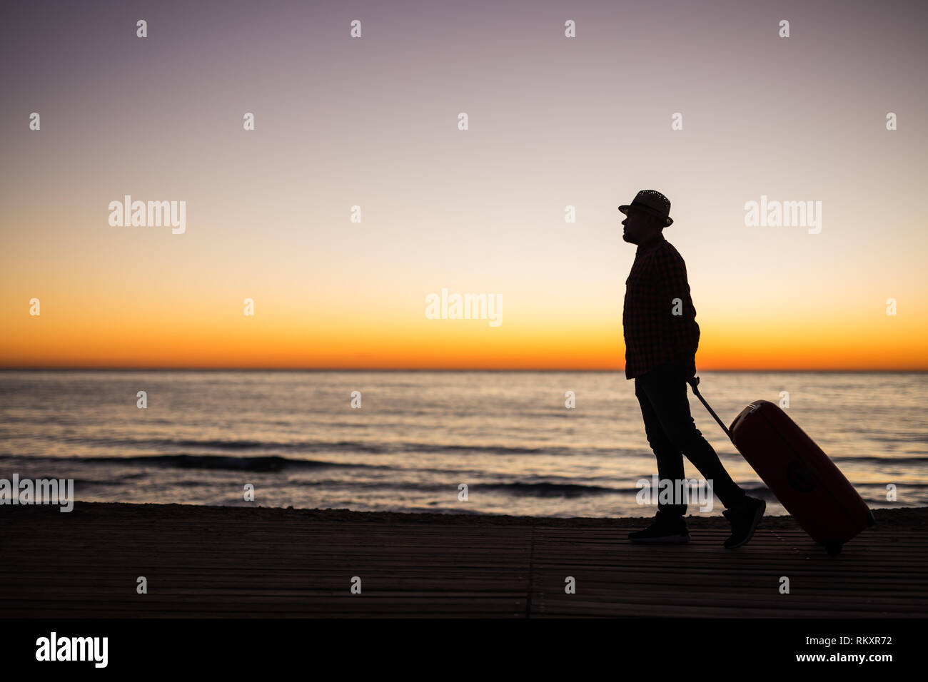 Vacances, l'été et travel concept - jeune homme d'ossature avec valise au coucher du soleil près de la mer Banque D'Images