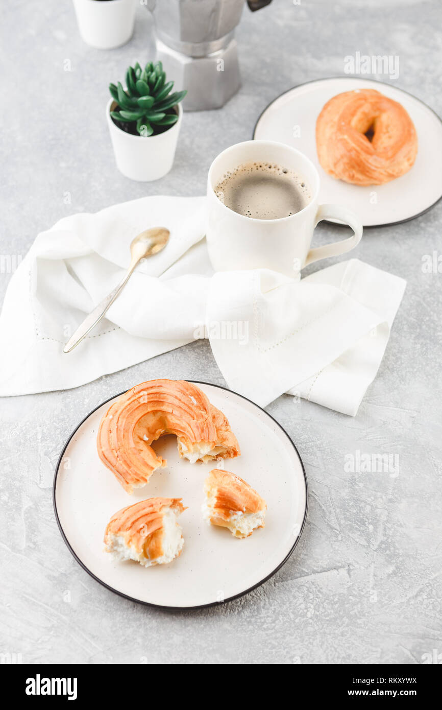 Le petit-déjeuner avec anneaux - chou à la crème, pâte à choux et tasse de café noir sur fond clair Banque D'Images