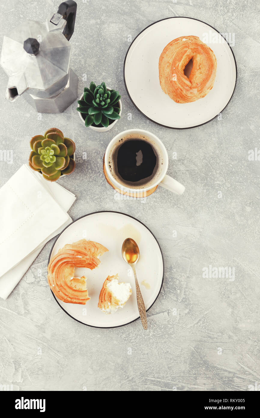 Le petit-déjeuner avec anneaux - chou à la crème, pâte à choux et tasse de café noir sur fond clair Banque D'Images