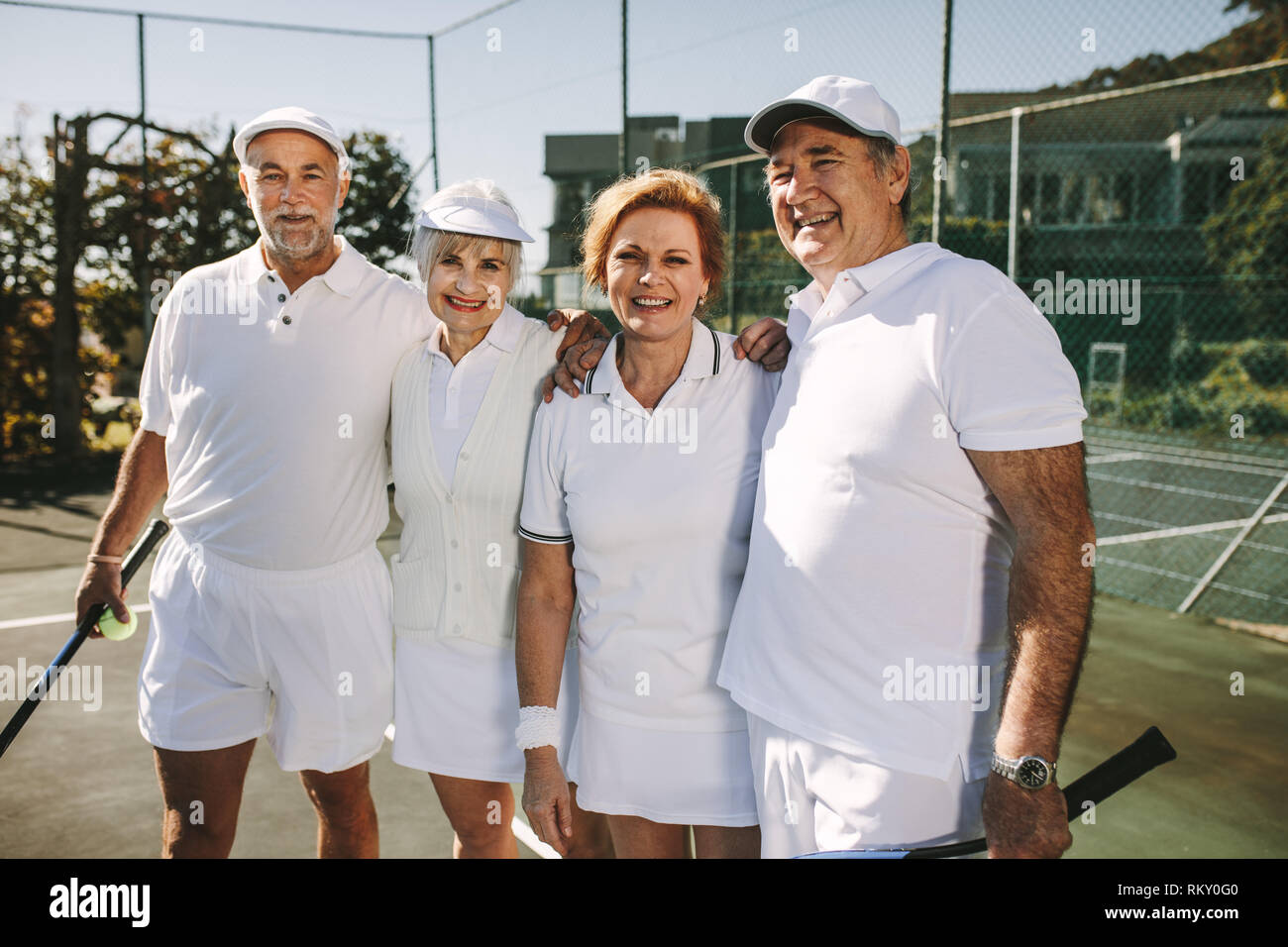 Les personnes âgées se tenant ensemble se tenant sur un court de tennis. Les aînés debout sur un court de tennis à jouer un match de double mixte. Banque D'Images