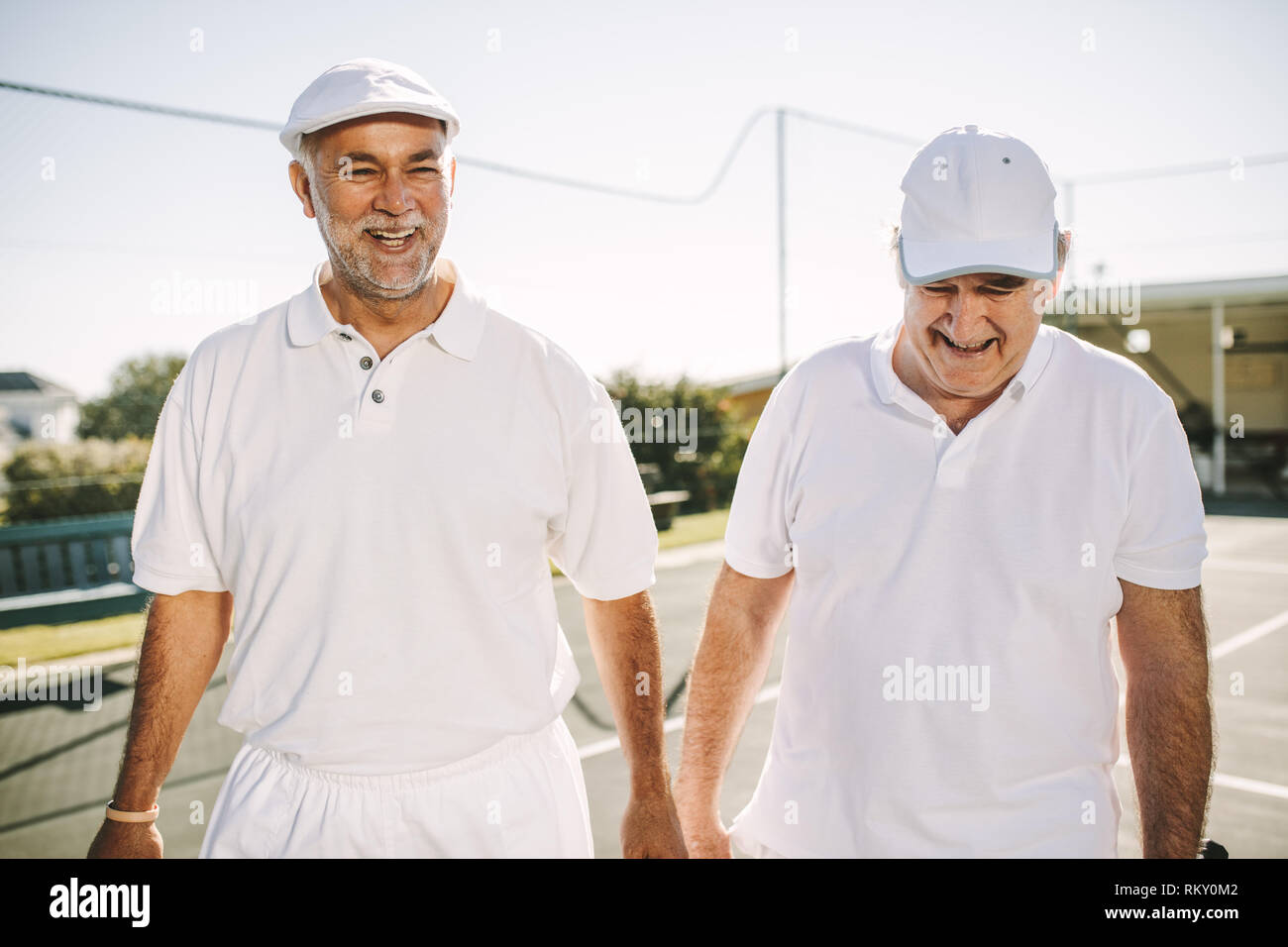 Smiling senior hommes en tennis porter parlent de la marche sur un court de tennis. Les hommes jouent au tennis sur une journée ensoleillée. Banque D'Images