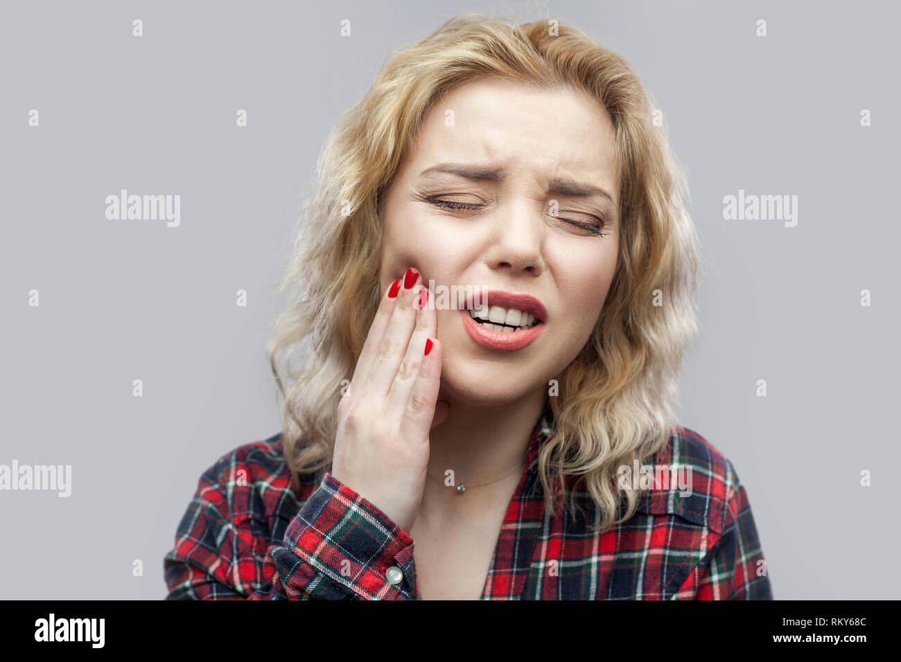 Mal de dent. Portrait de belle blonde jeune femme en chemise à carreaux rouge occasionnel et permanent lui touchant les dents douloureuses aux yeux clos. Piscine st Banque D'Images