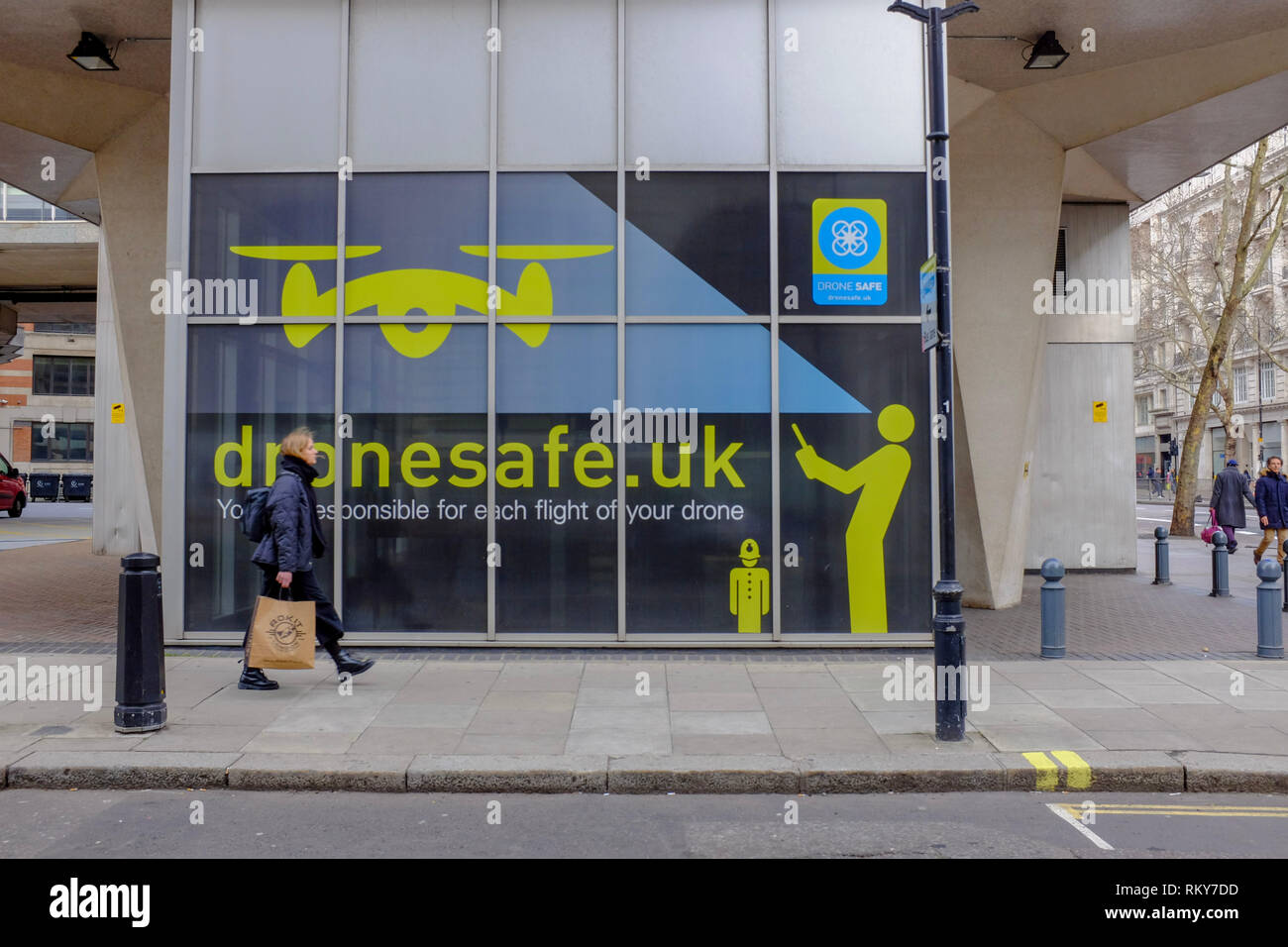 Londres, Royaume-Uni. 23 févr., 2019. Une femme passe devant un panneau opérateurs drone d'avertissement au sujet de la loi, peint à l'extérieur des bureaux de l'autorité de l'Aviation Civile Banque D'Images