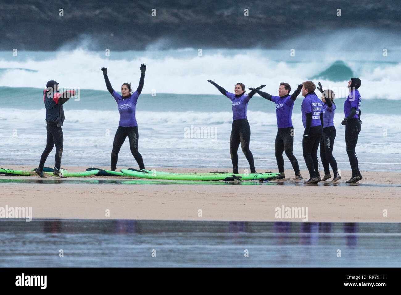 Les surfeurs débutants se réchauffer avec leur moniteur au début d'une leçon de surf à la plage de Fistral à Newquay en Cornouailles. Banque D'Images