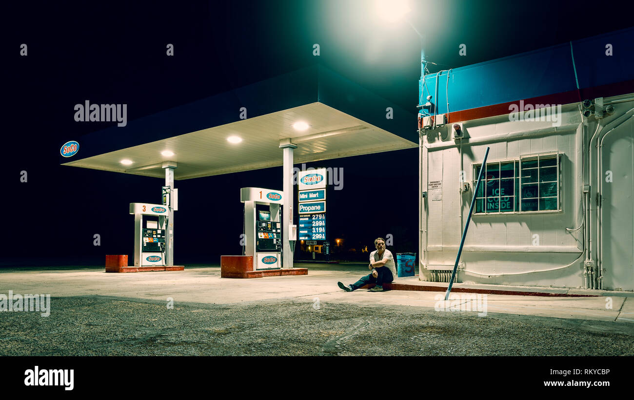 Homme est assis seul à une station d'essence fermée la nuit à Niland en Californie. Banque D'Images