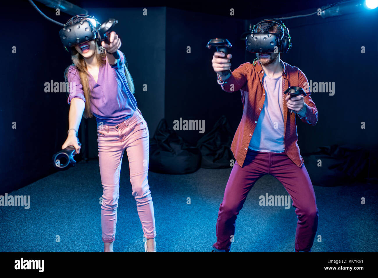 L'homme et de la femme joue une partie de l'utilisation de casque de réalité virtuelle et les manettes de jeu dans l'obscurité de la chambre club de lecture Banque D'Images