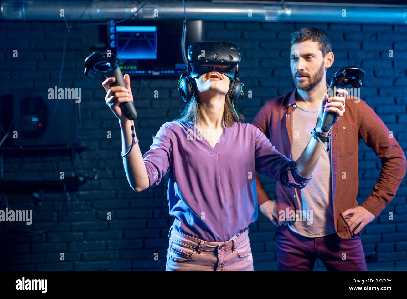 Jeune femme essayant casque de réalité virtuelle avec l'article avec l'homme assistant dans le club de lecture Banque D'Images