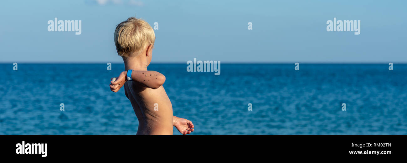 Voir l'échelle de l'image de blonde bébé garçon jeter pierre dans une belle mer bleue. Banque D'Images