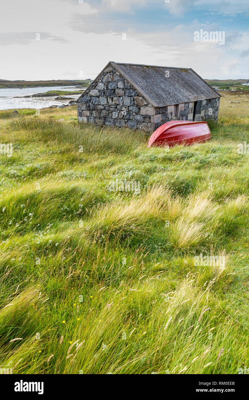 Chalet traditionnel en pierre rouge et bateau à rames par la côte, Uist, îles Hébrides, Ecosse, Royaume-Uni, Europe Banque D'Images