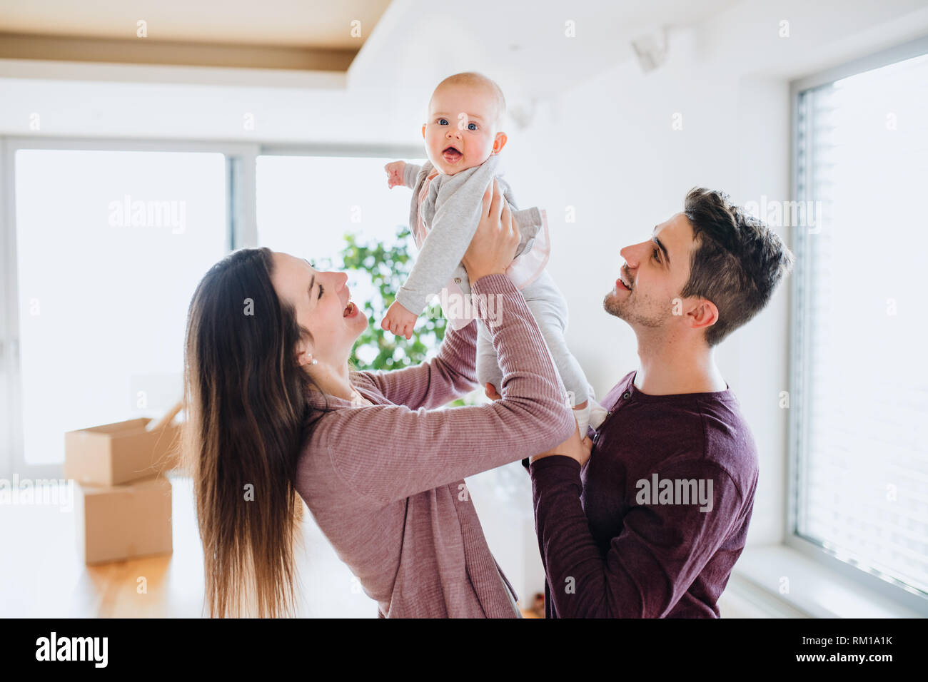 Portrait d'un jeune couple avec un bébé et des boîtes en carton déménagement dans une nouvelle maison. Banque D'Images