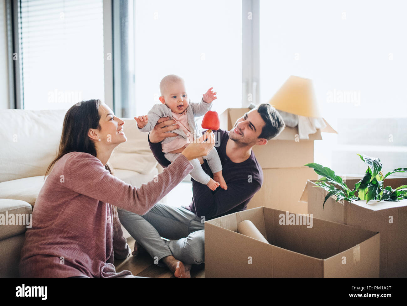 Portrait d'un jeune couple avec un bébé et des boîtes en carton déménagement dans une nouvelle maison. Banque D'Images