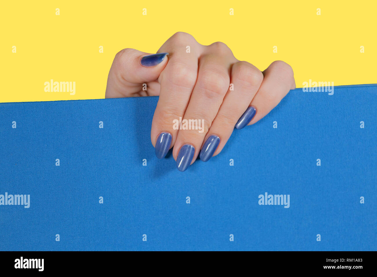 Libre Vue de dessus de main de femme blanc avec brillant brillant gel bleu moderne polonais. Les ongles manucurés de macro de femme adulte isolé sur le jaune et bleu ba Banque D'Images