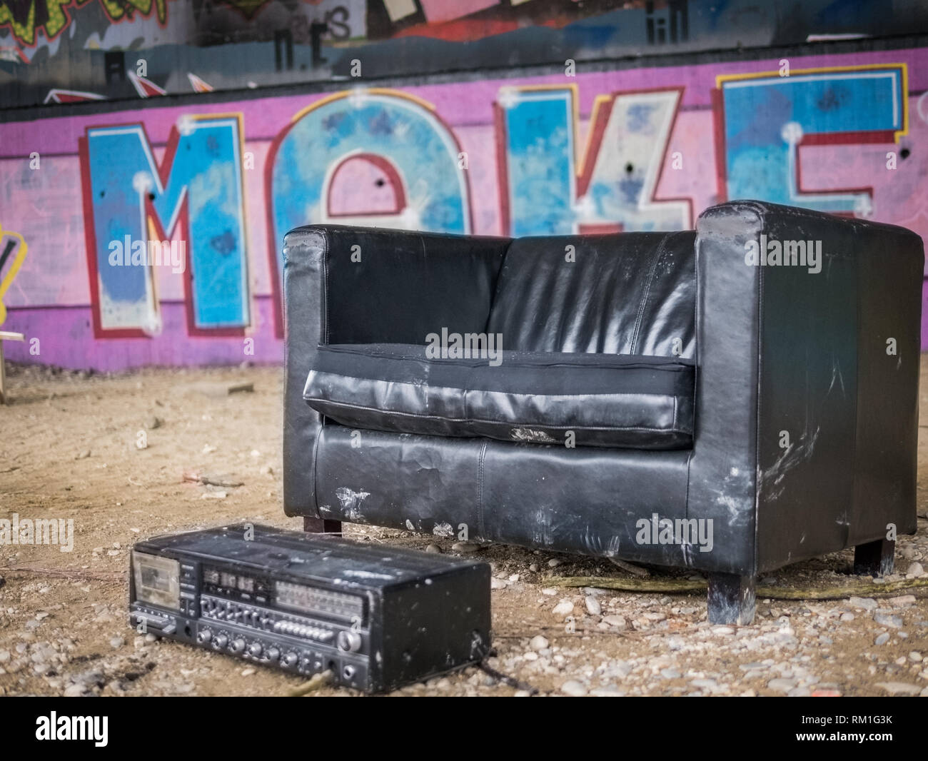 Fauteuil en cuir noir et vieille radio dans un refuge créatif réfrigérés sous un pont avec des graffitis en arrière-plan Banque D'Images
