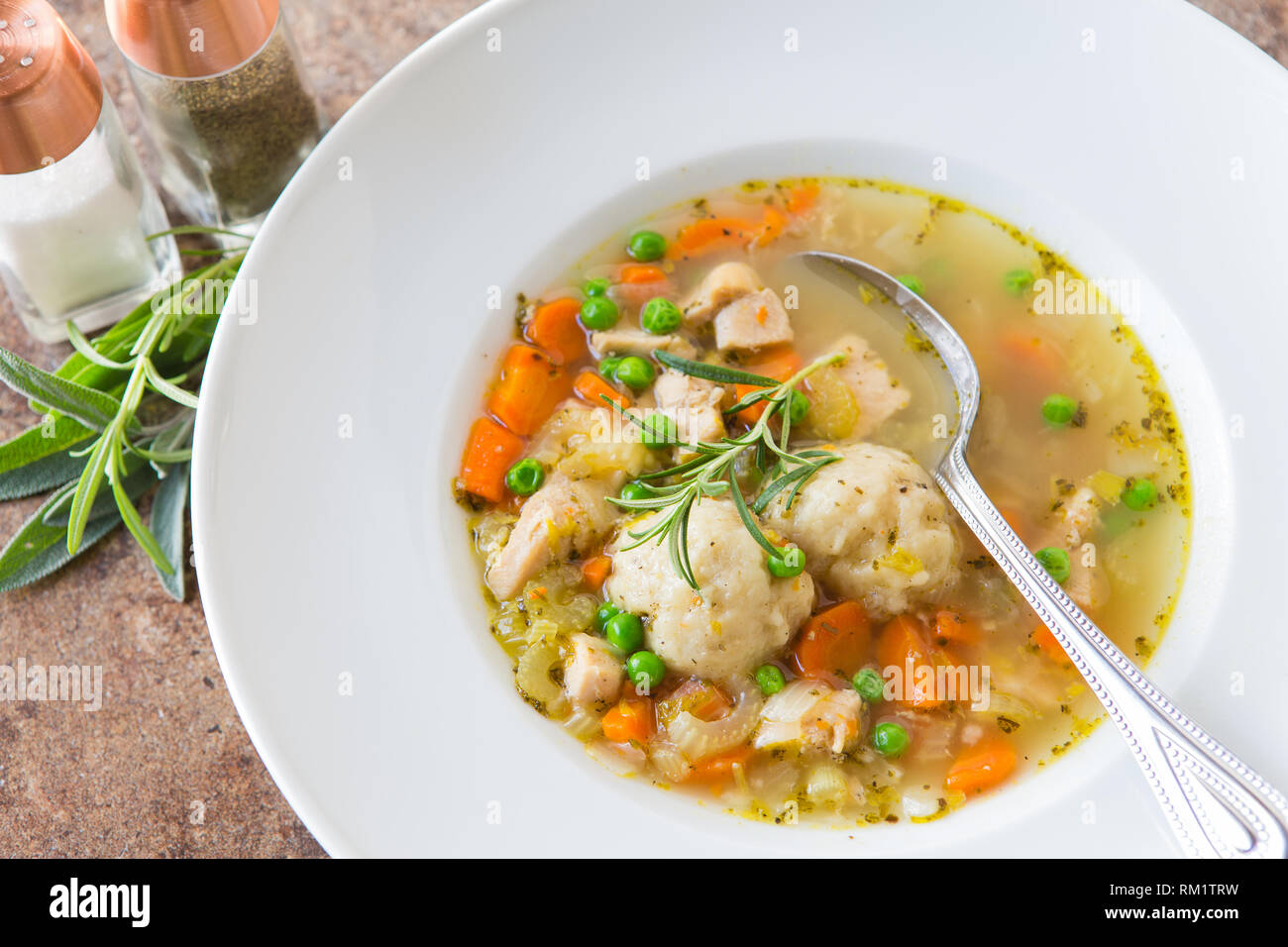 Soupe au poulet fait maison avec des légumes frais et des boulettes faites maison servi dans un bol blanc avec salières et poivrières et herbes fraîches. Banque D'Images