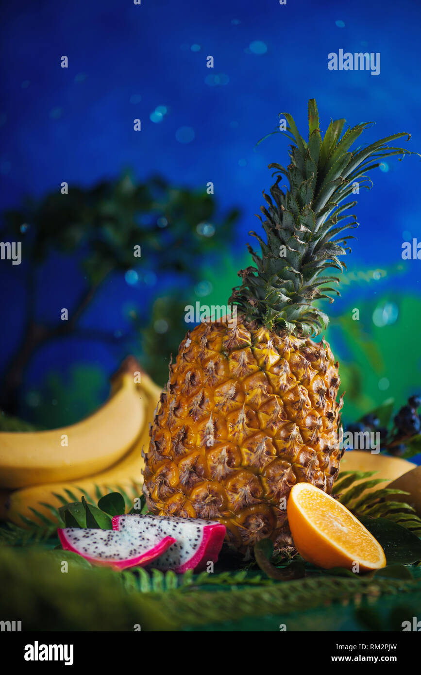Ananas, bananes, mangues, fruit du dragon avec feuilles tropicales sur un fond bleu avec des gouttes d'eau et de l'espace de copie Banque D'Images