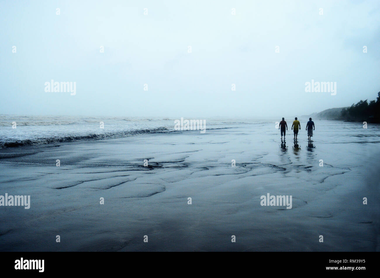 Trois hommes marchant dans la solitude sur une plage Banque D'Images