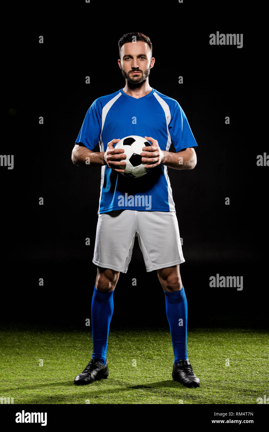 Joueur de football avec ballon permanent on Green grass isolated on black Banque D'Images