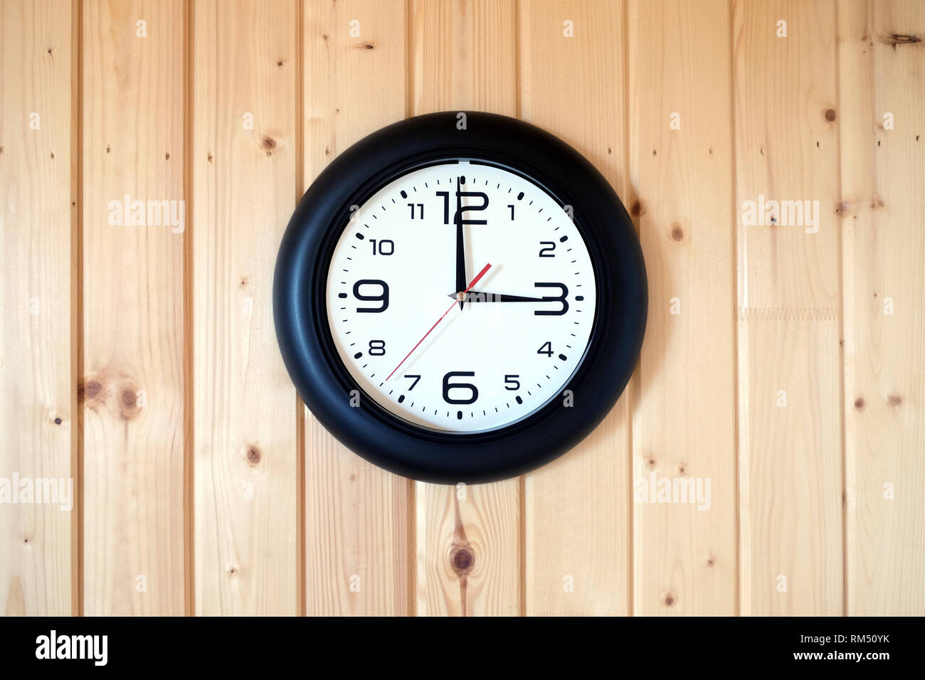 Grande horloge murale ronde avec une jante noire avec des flèches montrant trois heures s'interrompt sur le mur en bois brun à partir de planches verticales à l'intérieur sur fond de bois Banque D'Images