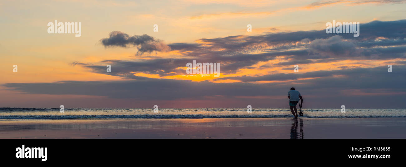 L'homme prend la mer sur vidéo. Panorama, bannière, format long de coucher de soleil sur la plage de Kuta avec reflet dans l'eau sur l'île de Bali Banque D'Images
