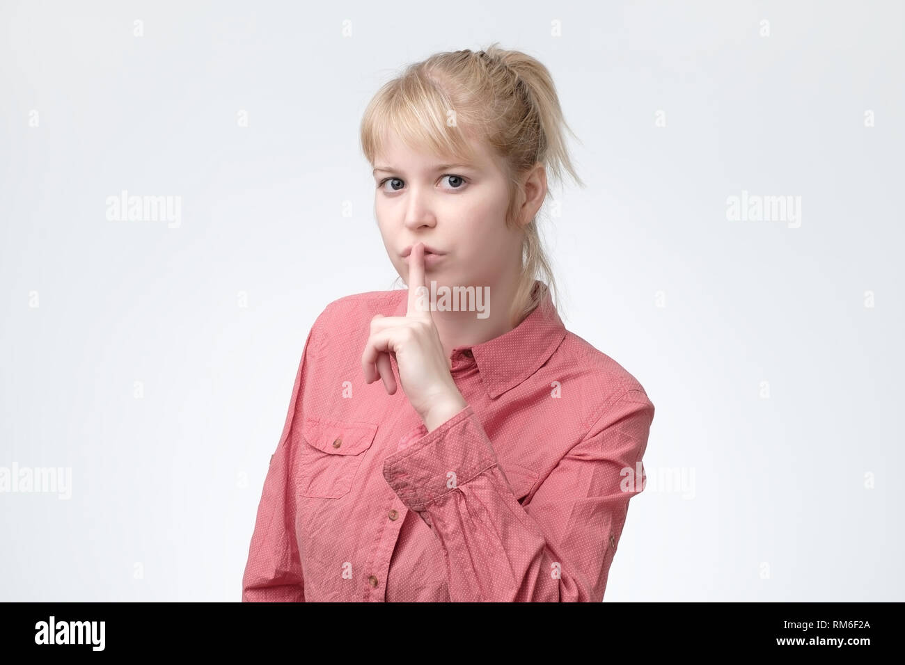 Ovely blonde vous demande de garder le secret des renseignements confidentiels, vêtus de t-shirt rose Banque D'Images