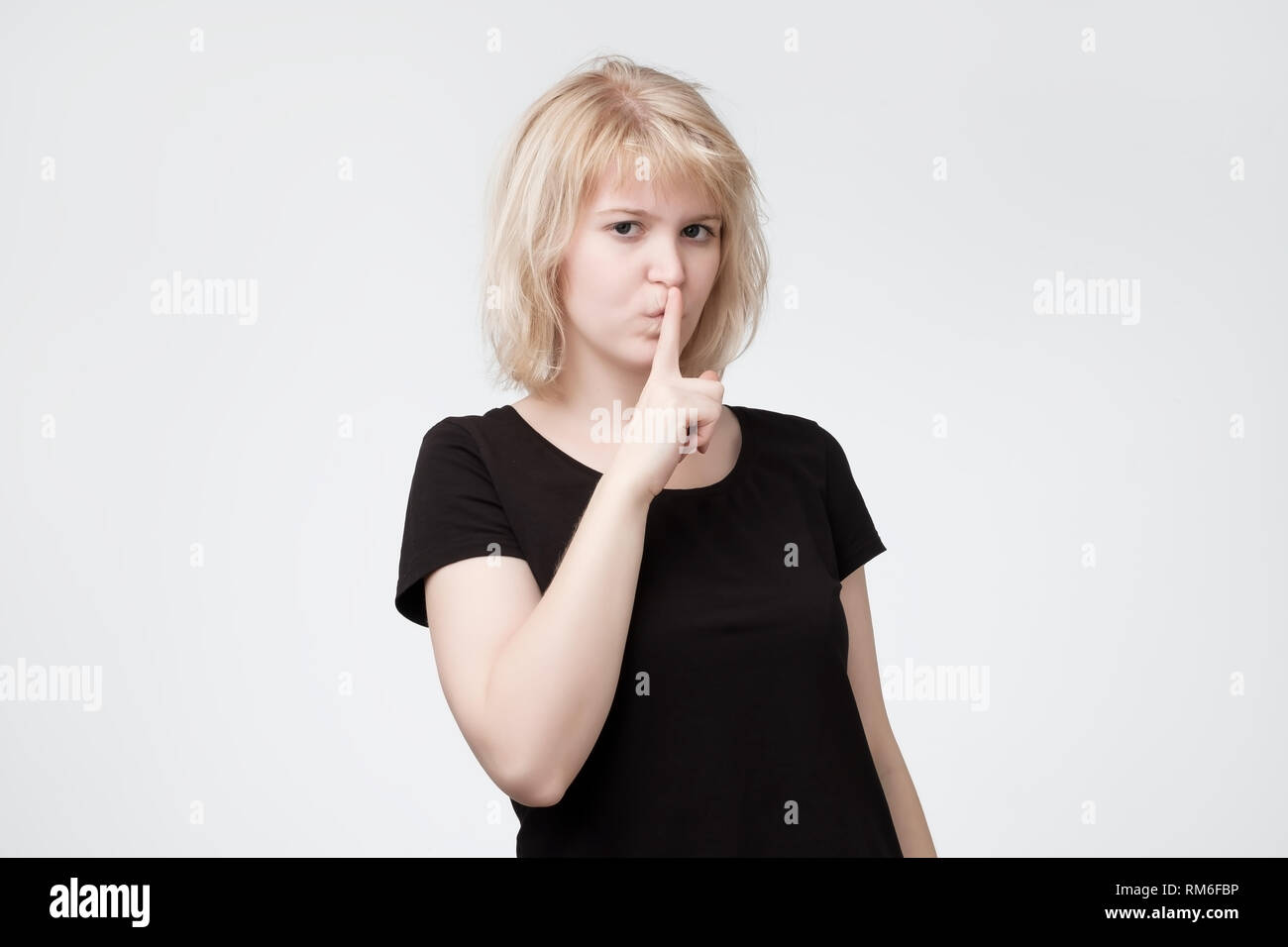 Ovely blonde vous demande de garder le secret des renseignements confidentiels, vêtus de t-shirt noir Banque D'Images