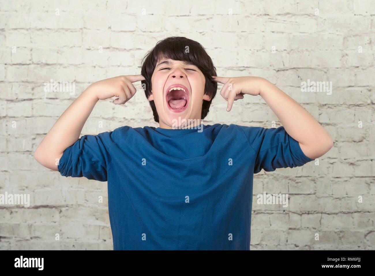 Portrait de jeune garçon en colère crier sur fond brique Banque D'Images