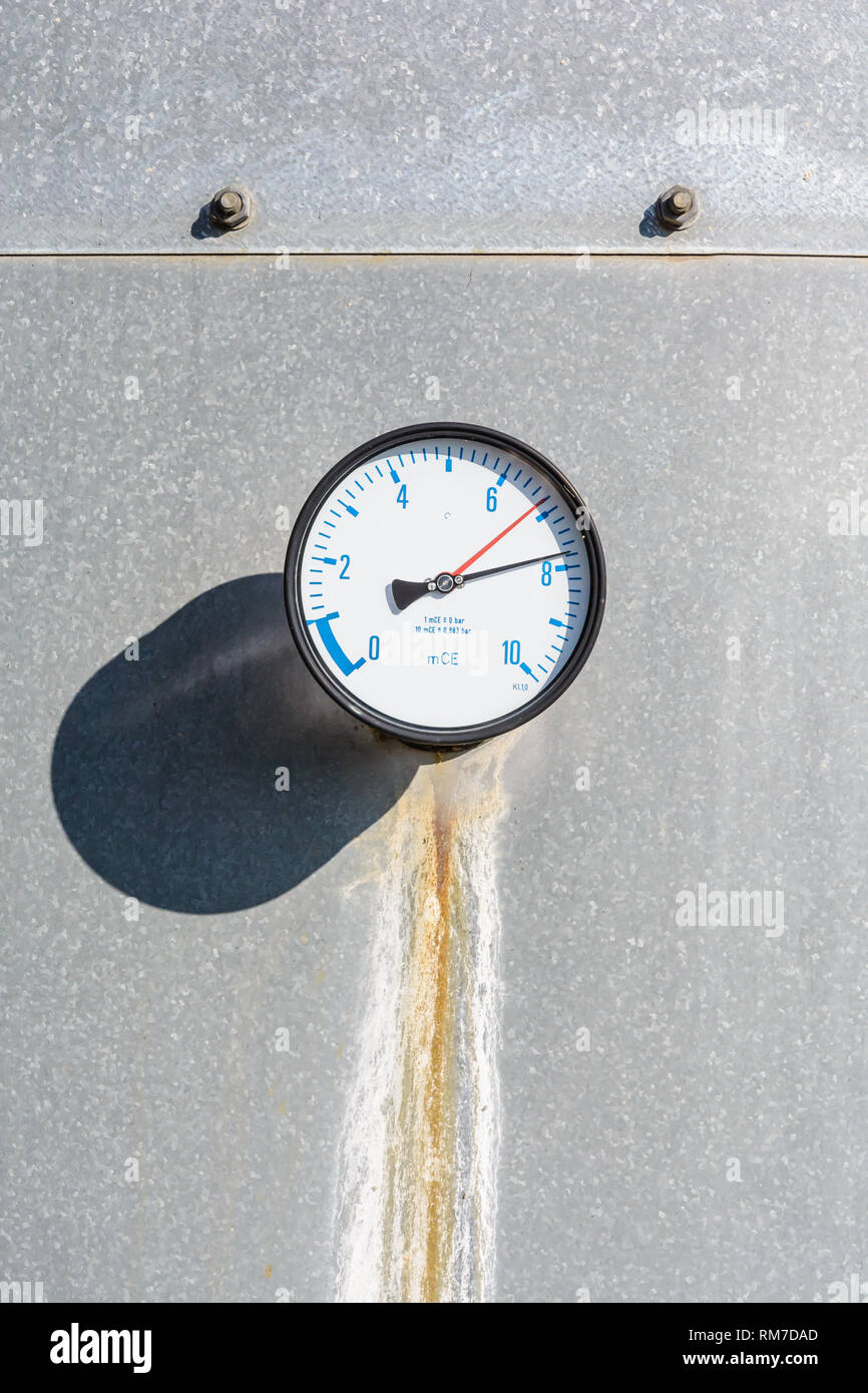 Close-up of a round manomètre avec une strie sec fonctionnant en bas ci-dessous, monté sur le mur d'un réservoir d'eau en acier galvanisé, avec chiffres en bleu sur un cadran blanc Banque D'Images