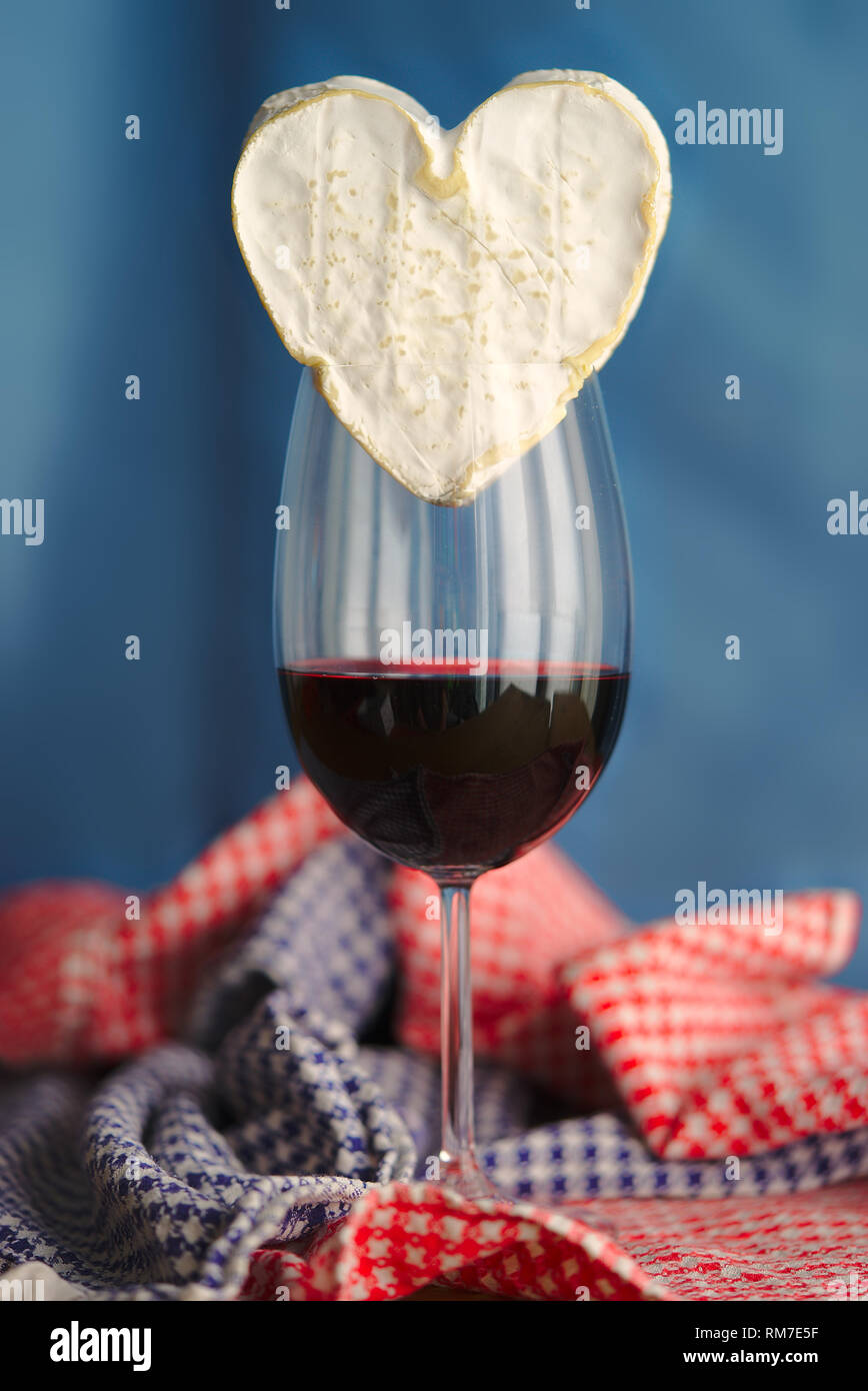 La composition avec Neufchatel, fromage normand (A.O.P.) et d'un verre de vin, sur un fond bleu. Banque D'Images