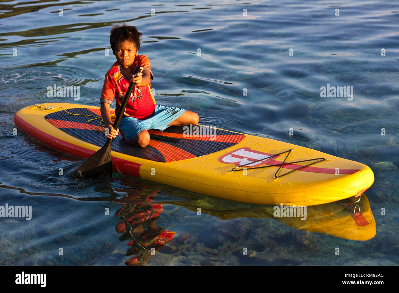 Un garçon MOKEN sur un paddle board le long de la côte de Ko Surin île thaïlandaise dans le parc national de Mu Koh Surin - Thaïlande Banque D'Images