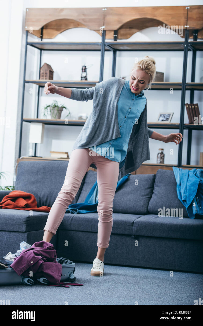 Femme en colère en poussant les vêtements dans une valise à jambe après sa rupture avec petit ami Banque D'Images