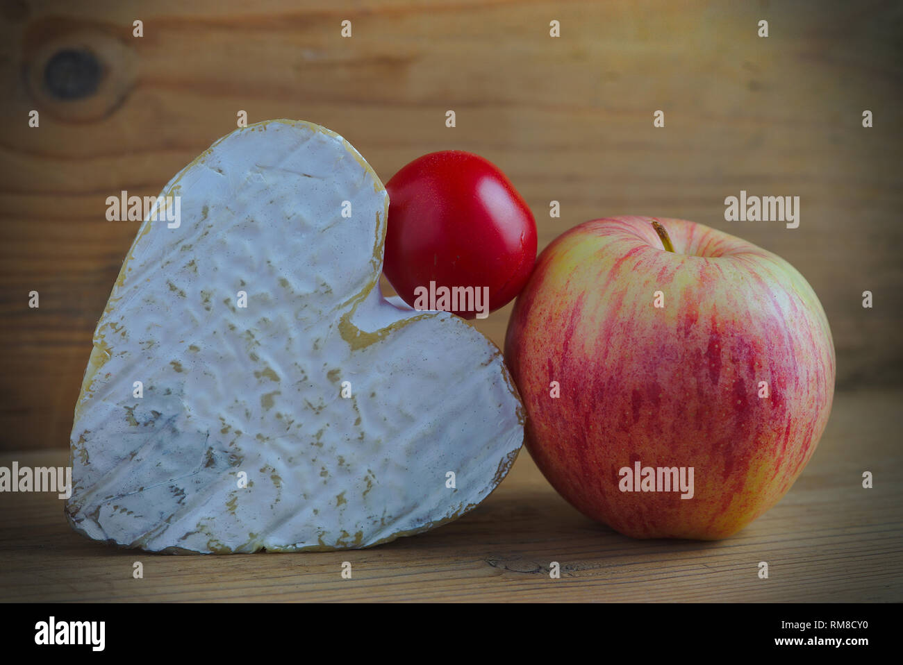 Nature morte avec un fromage Neufchatel (Norman A.O.P.) une tomate cerise et une pomme sur fond de bois Banque D'Images